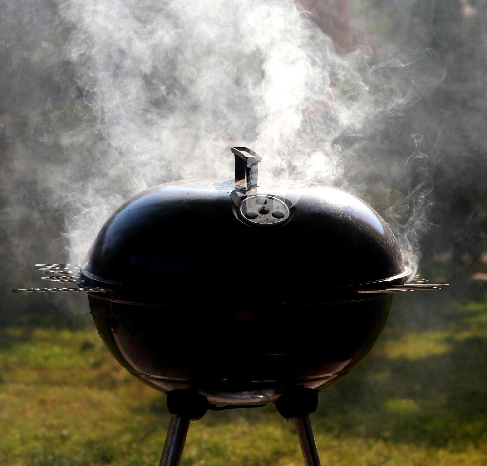 Capture of a smoking barbecue grill outdoors, emitting steam on a bright sunny day.